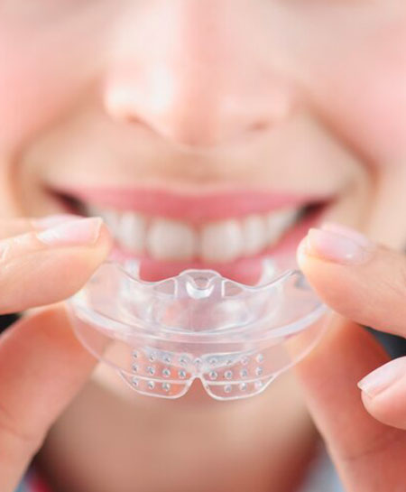 Mujer sonriente sostiene protector bucal de plástico transparente para enderezar dientes